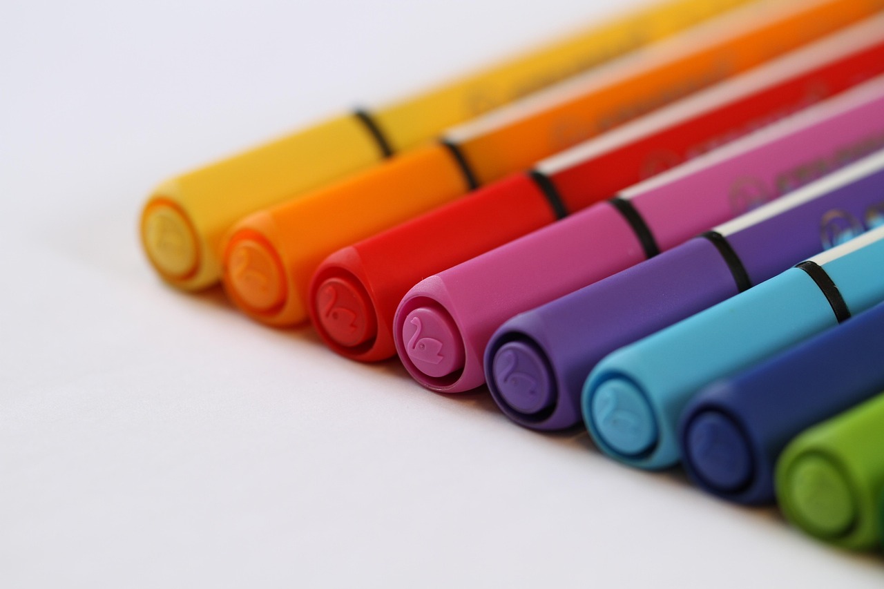 A row of colorful pens arranged neatly on a white surface, showcasing various hues and designs.